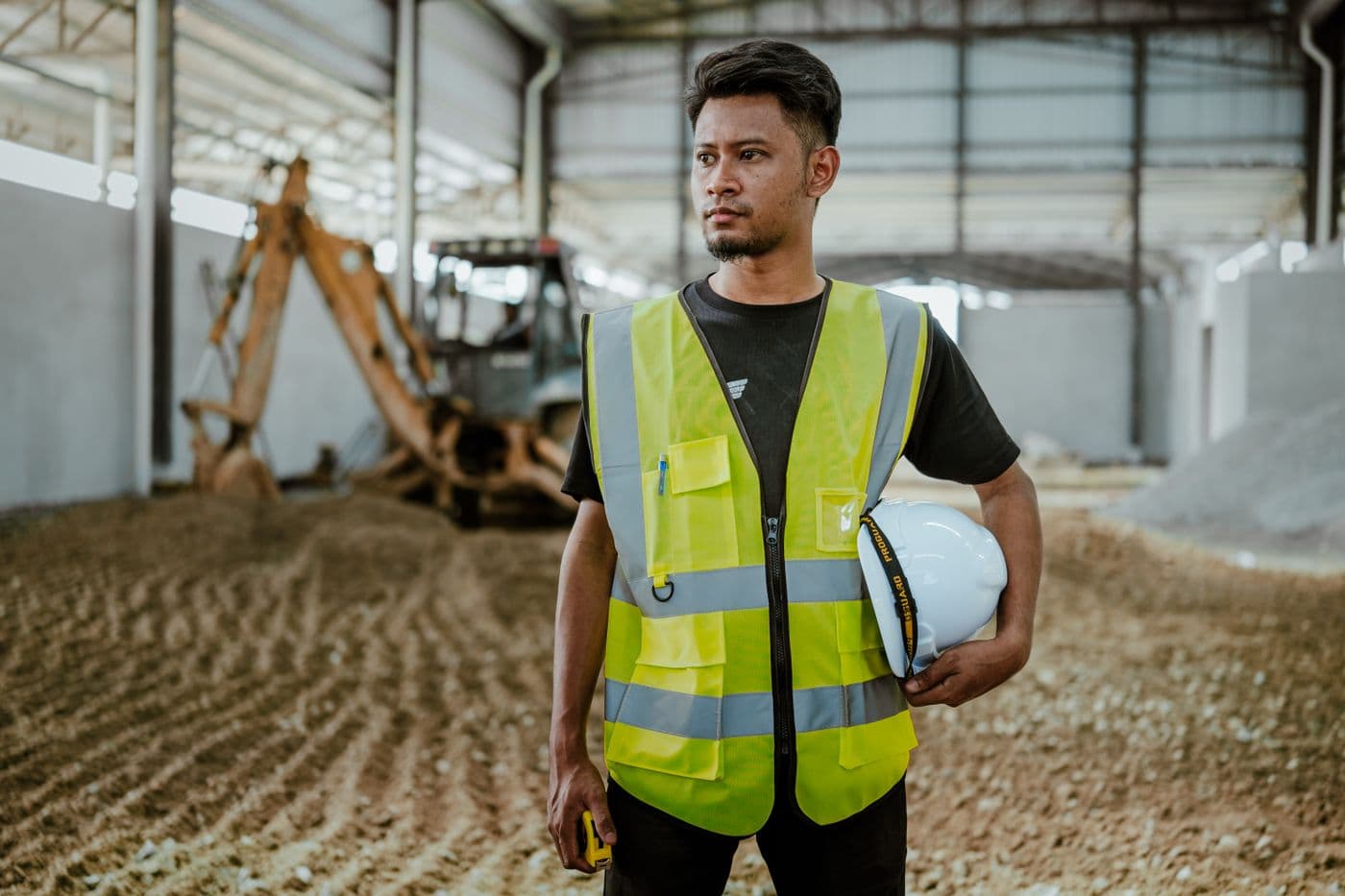 Construction worker in a high-visibility vest holding a hard hat on site