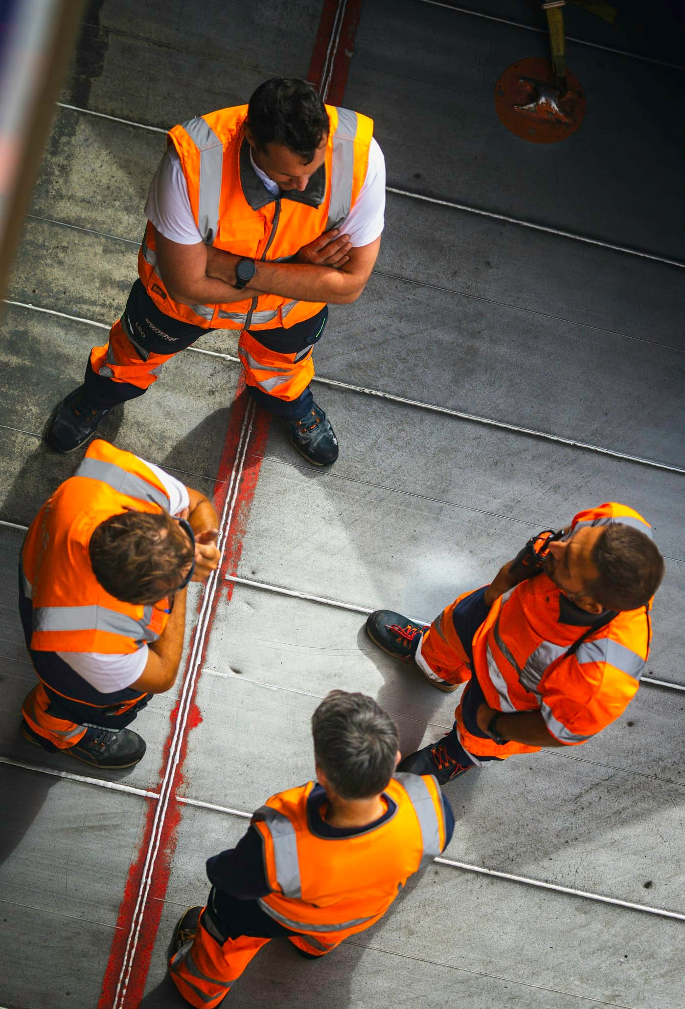 Workers in orange high-visibility vests on a factory floor, seen from above