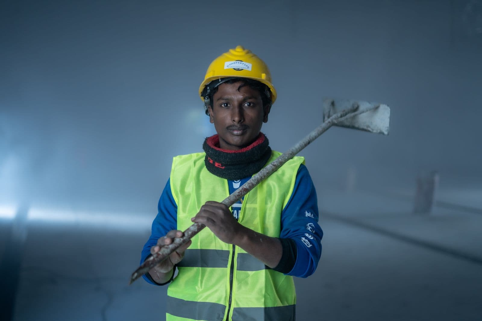 Worker in a hard hat and high-visibility vest holding a tool on an industrial site